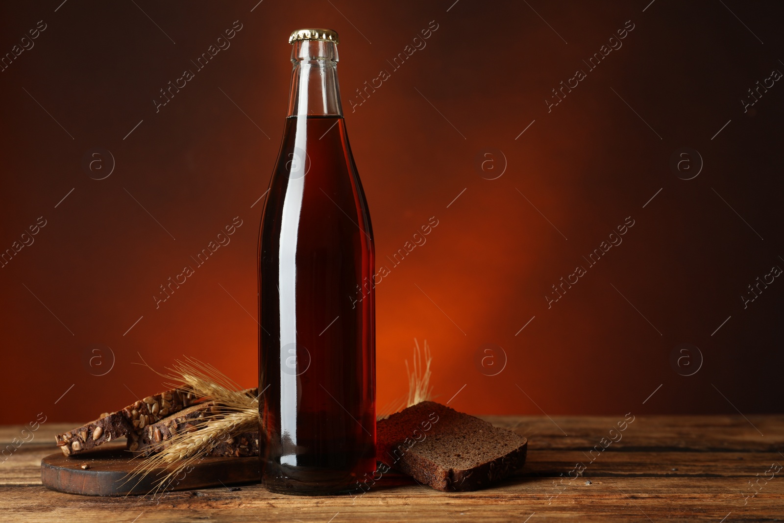 Photo of Bottle of delicious fresh kvass, spikelets and bread on wooden table. Space for text