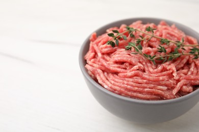 Fresh raw ground meat and thyme in bowl on white table, closeup. Space for text