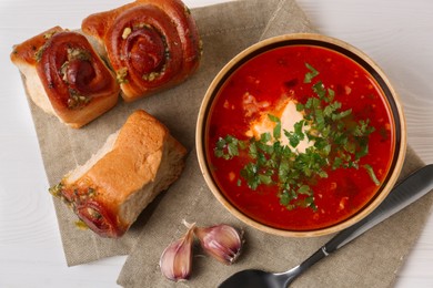 Photo of Delicious borsch served with pampushky on white wooden table, top view. Traditional Ukrainian cuisine