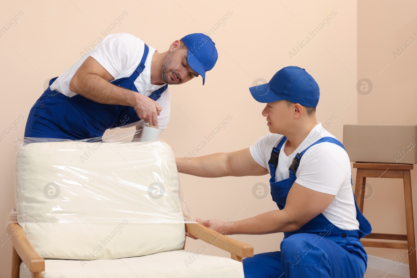 Photo of Workers wrapping armchair in stretch film indoors