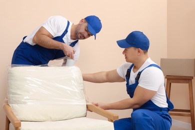 Photo of Workers wrapping armchair in stretch film indoors