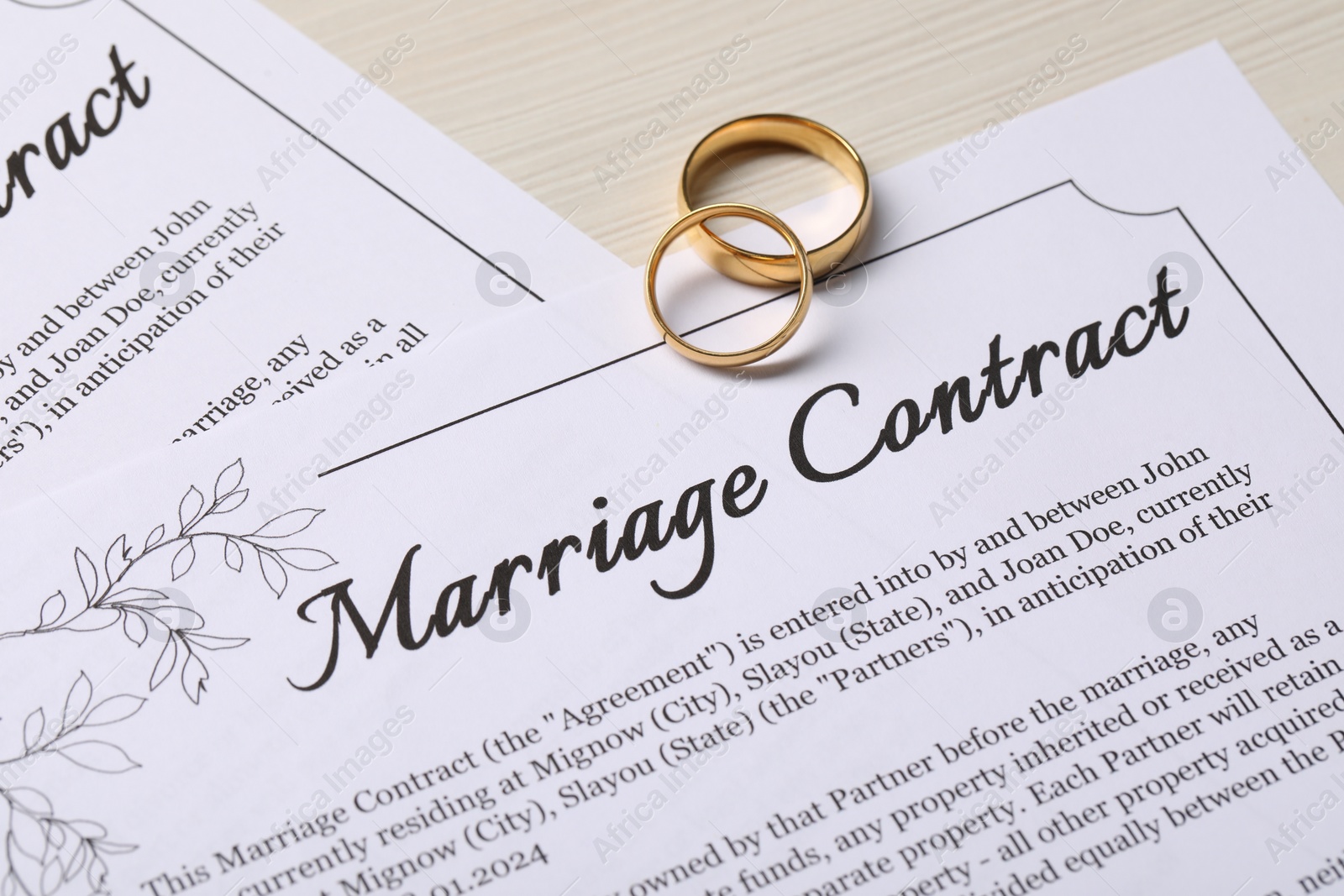 Photo of Marriage contracts and gold rings on light wooden table, closeup