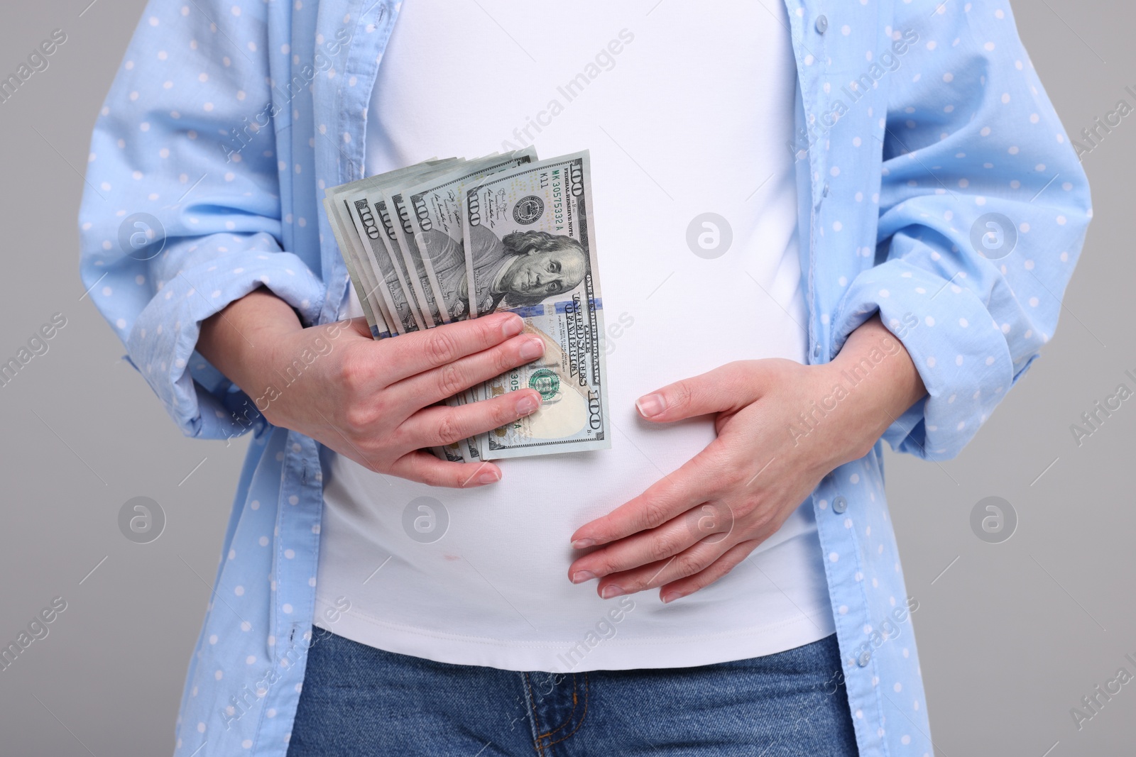 Photo of Surrogate mother. Pregnant woman with dollar banknotes on light grey background, closeup