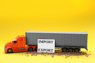 Photo of Card with words Import and Export, wheat grains near toy truck on yellow background