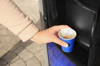 Photo of Woman taking paper cup with coffee from vending machine outdoors, closeup