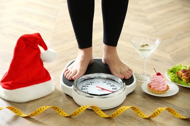 Photo of Food, alcohol left after Christmas holidays and woman with measuring tape standing on scales indoors, closeup. Overweight problem
