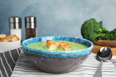 Photo of Delicious broccoli cream soup served on table against blue background. Space for text