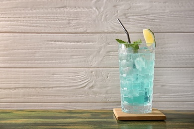 Photo of Glass with delicious cocktail and ice cubes on table against wooden background