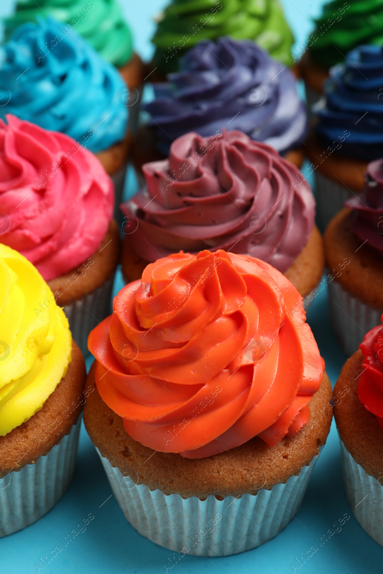 Photo of Many delicious colorful cupcakes on light blue background, closeup