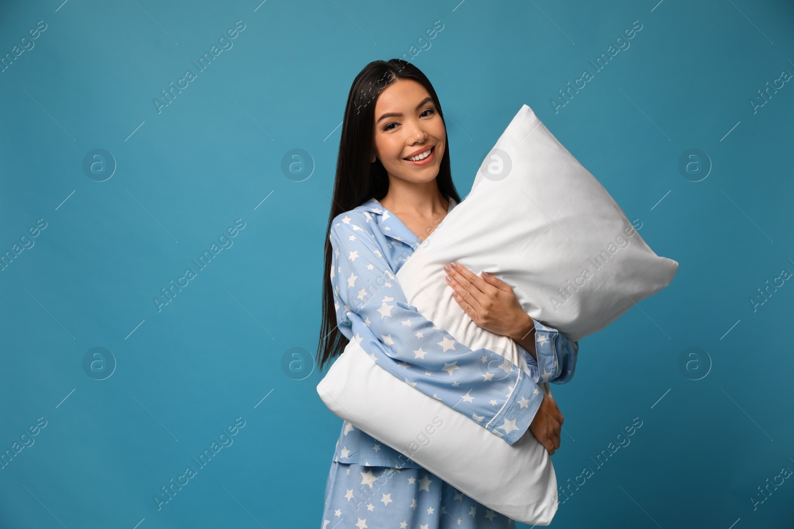 Photo of Beautiful Asian woman with pillow on blue background. Bedtime