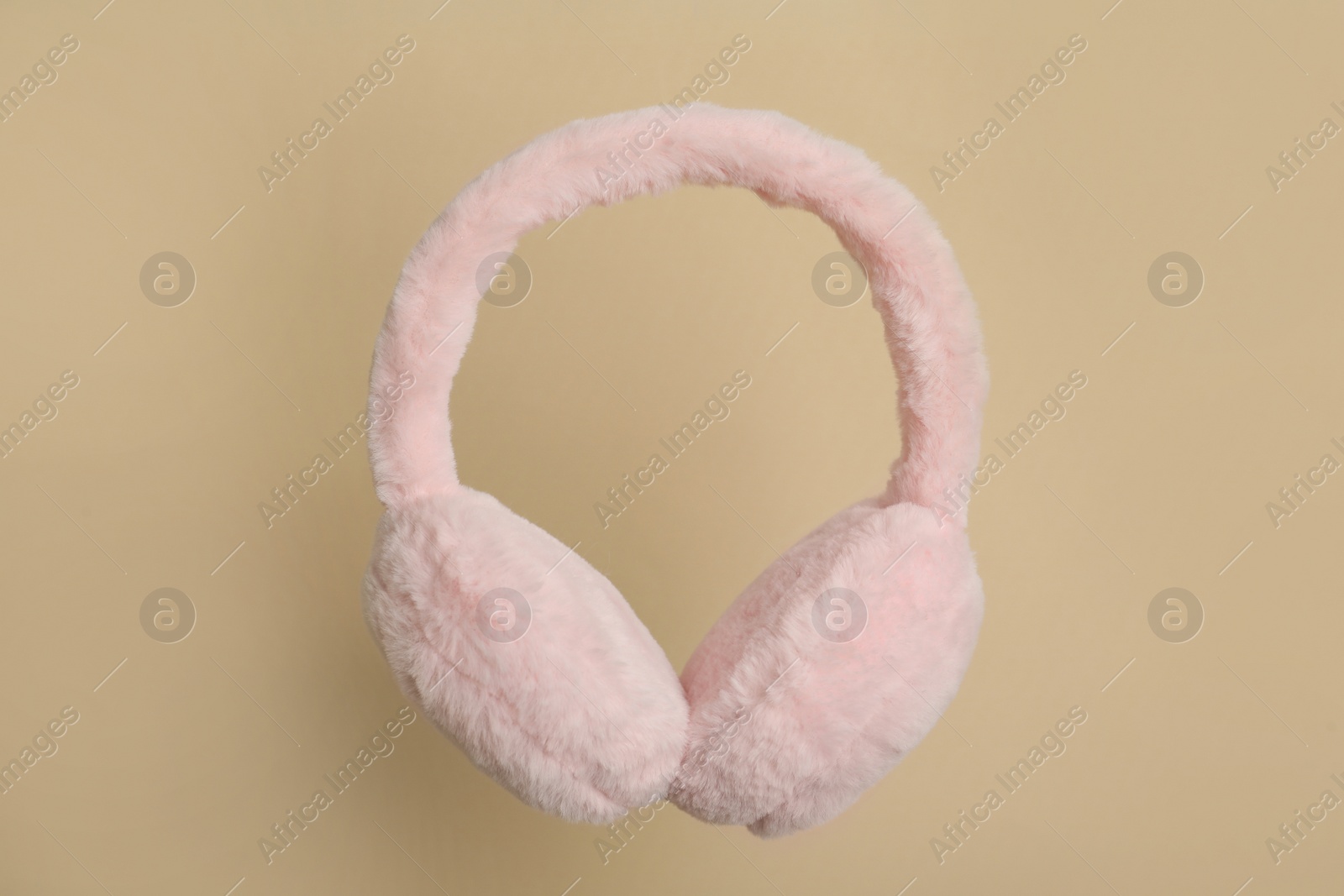 Photo of Fluffy earmuffs on beige background. Stylish winter accessory