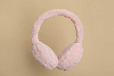 Photo of Fluffy earmuffs on beige background. Stylish winter accessory