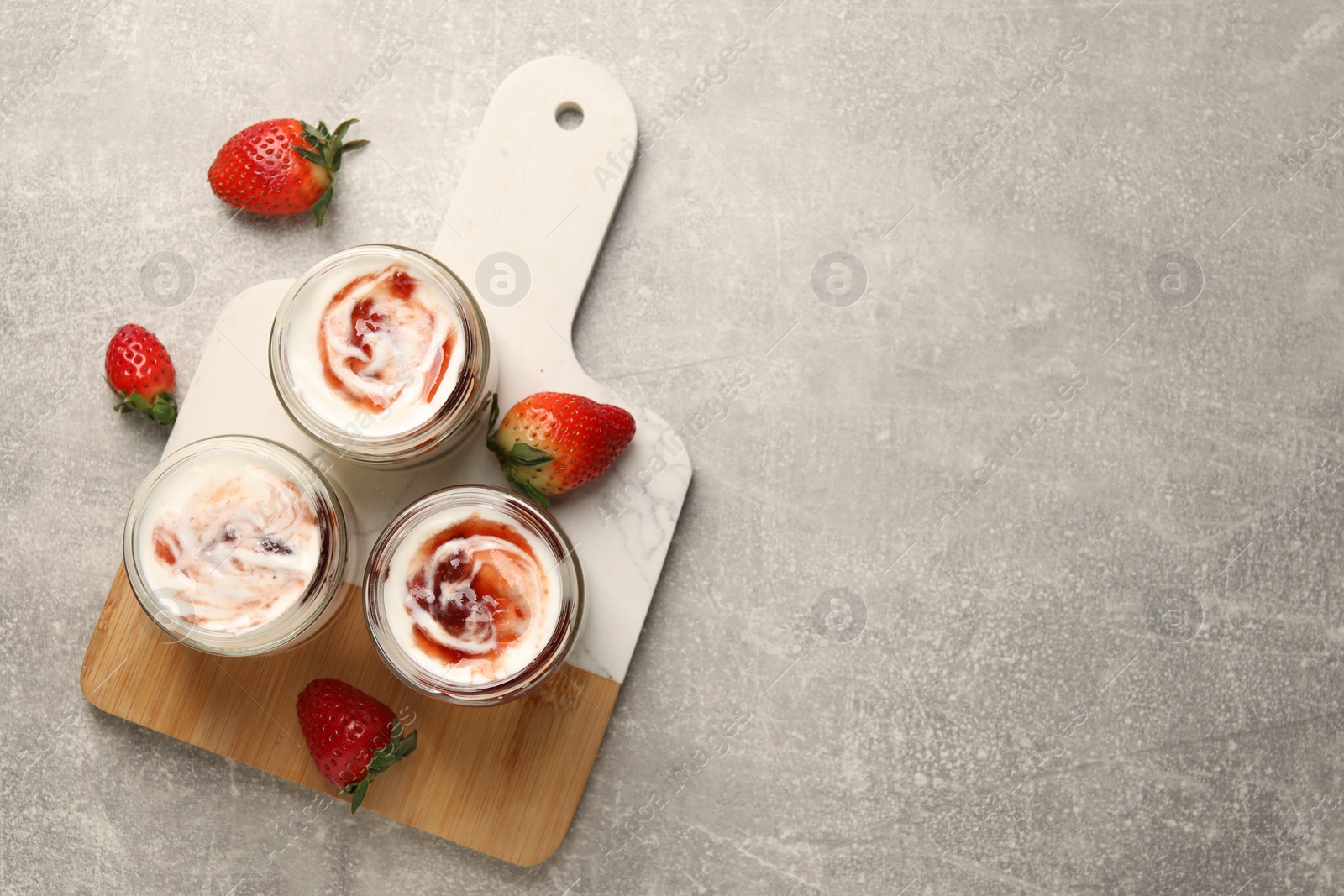 Photo of Tasty yoghurt with jam and strawberries on grey table, top view. Space for text