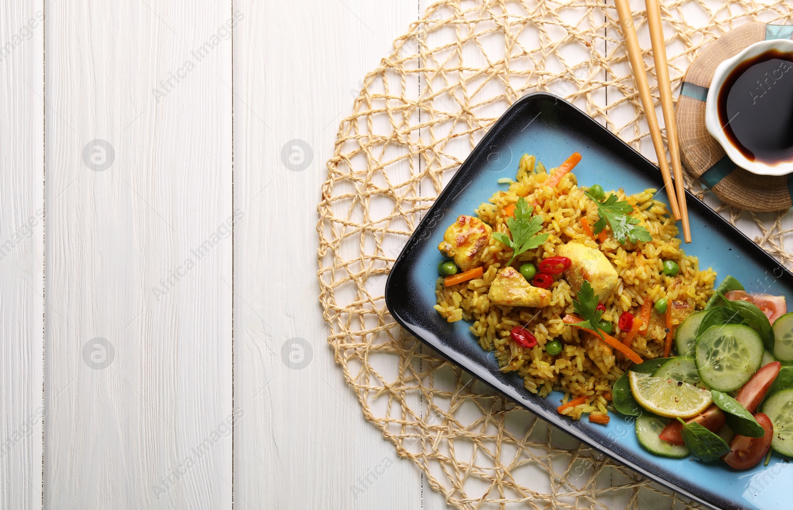 Photo of Tasty rice with meat and vegetables in plate near soy sauce on white wooden table, flat lay. Space for text