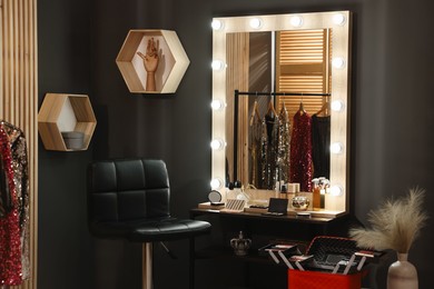 Makeup room. Stylish mirror near dressing table with beauty products and chair indoors