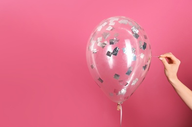 Woman piercing balloon with needle on color background, closeup. Space for text