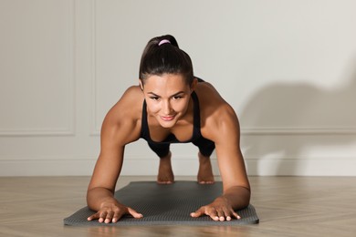 Photo of Young woman doing plank exercise near white wall