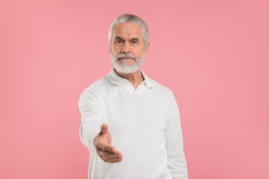Senior man welcoming and offering handshake on pink background