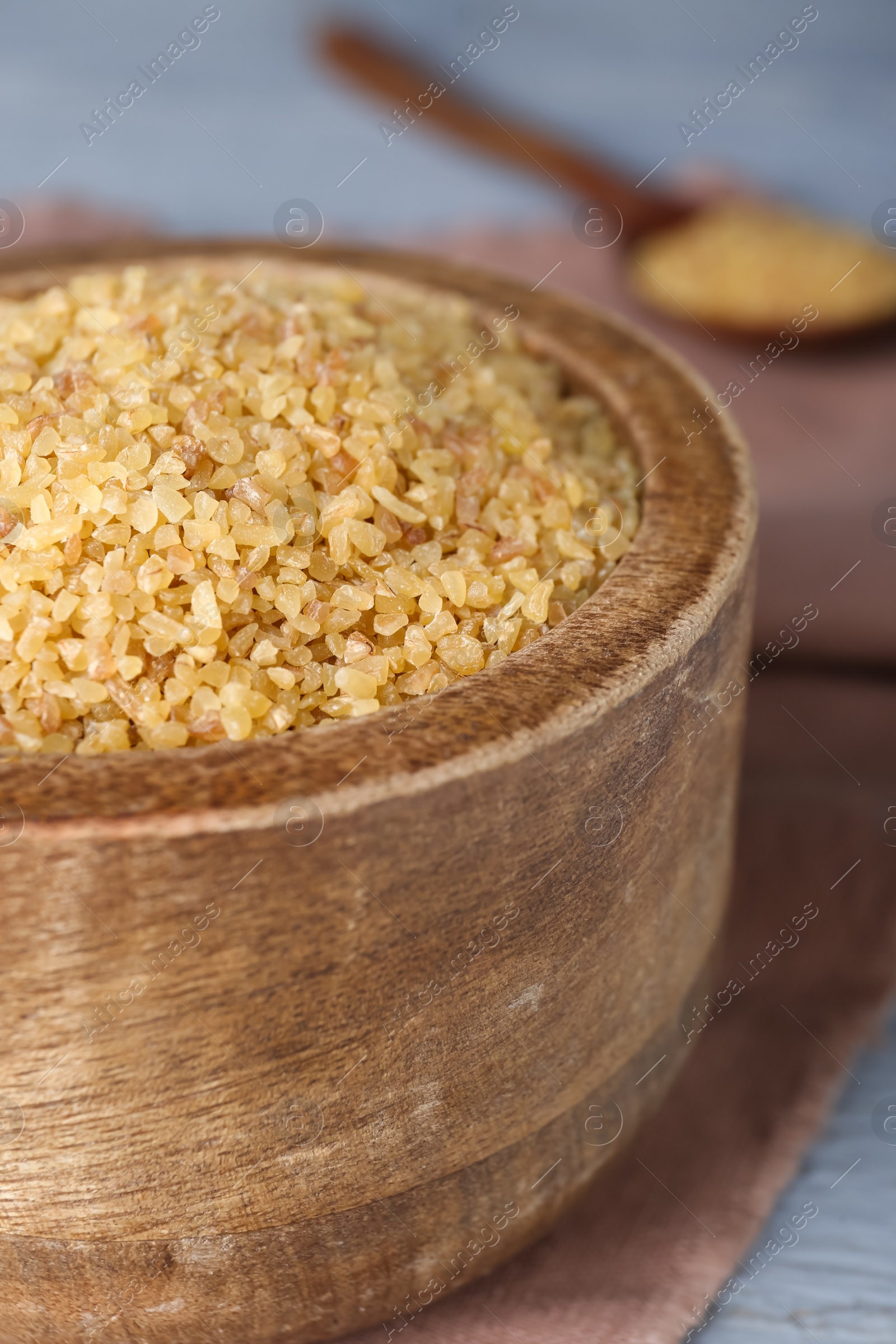 Photo of Wooden bowl with uncooked bulgur on grey table, closeup