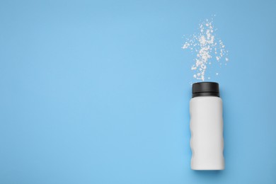 Photo of Bottle and scattered dusting powder on light blue background, top view with space for text. Baby cosmetic product