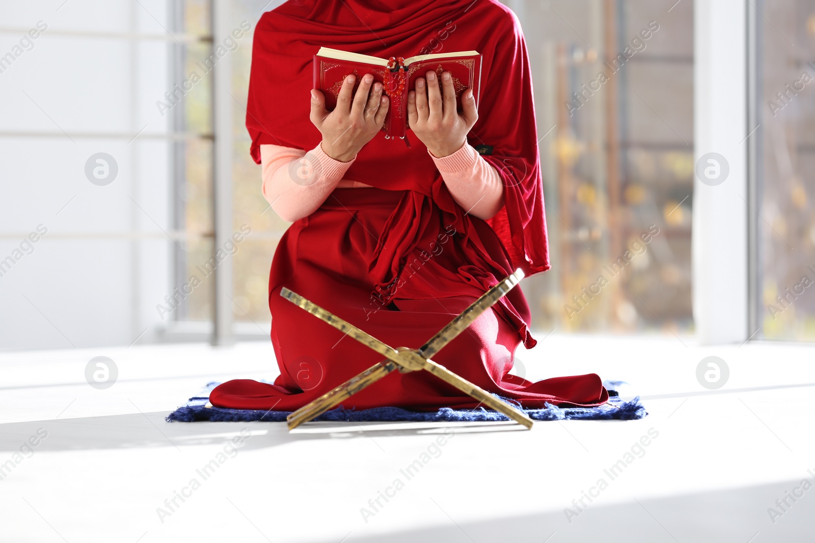 Photo of Muslim woman reading Koran on mat indoors, closeup