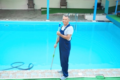 Photo of Male worker cleaning outdoor pool with underwater vacuum