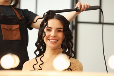 Hair styling. Hairdresser curling woman's hair in salon, closeup