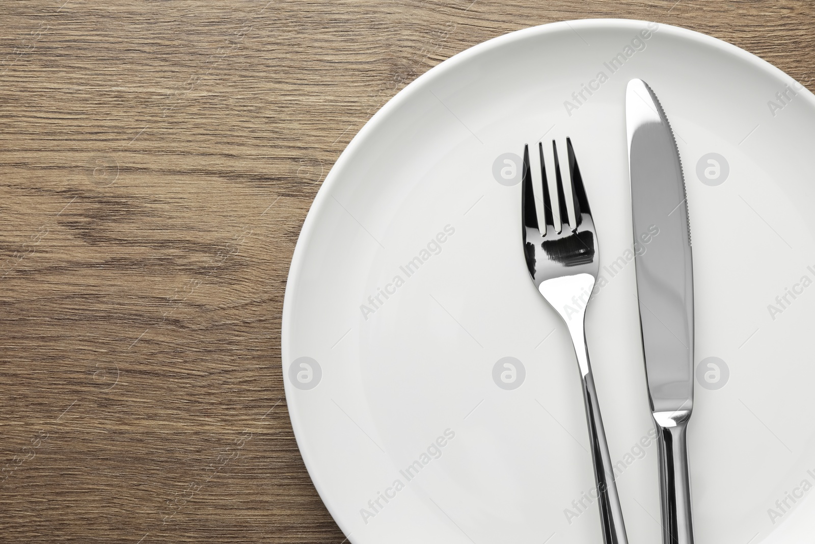 Photo of Plate, fork and knife on wooden table, top view. Space for text