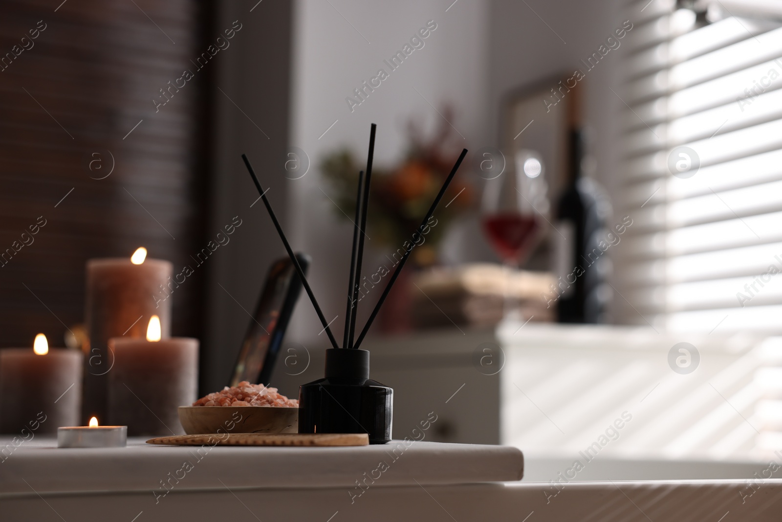 Photo of White wooden tray with burning candles, aroma diffuser and sea salt on bathtub in bathroom, space for text