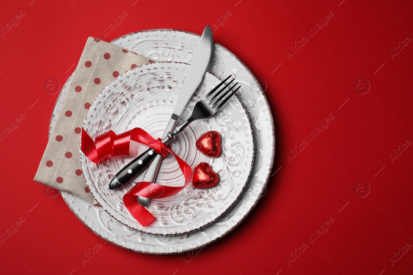 Photo of Beautiful place setting with dishware and sweets for romantic dinner on red table, top view