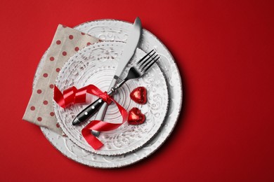 Beautiful place setting with dishware and sweets for romantic dinner on red table, top view