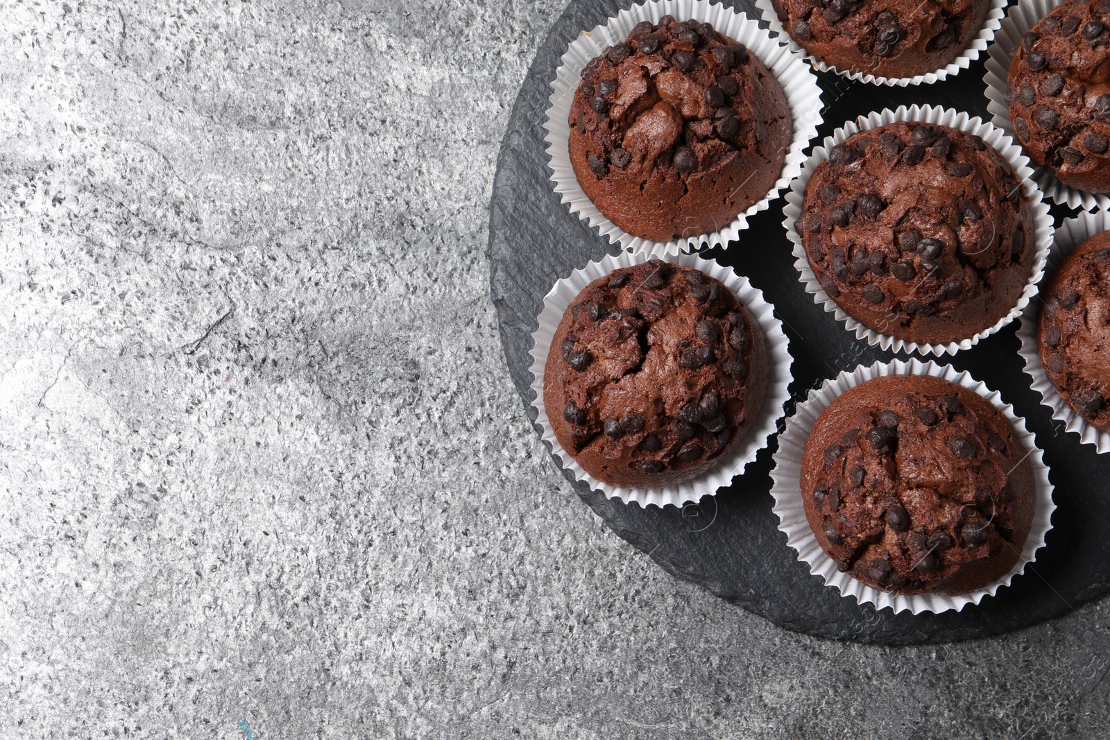 Photo of Tasty chocolate muffins on grey textured table, top view. Space for text