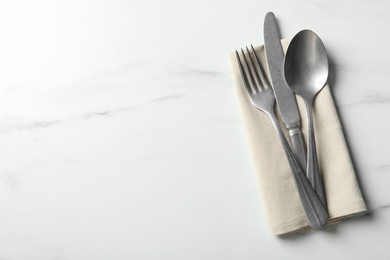 Set of stylish cutlery and napkin on white marble table, top view. Space for text