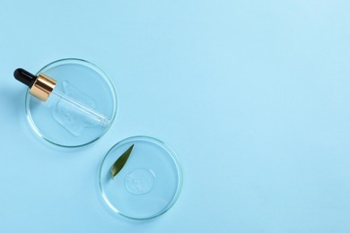 Photo of Petri dishes with samples of cosmetic oil, pipette and green leaf on light blue background, flat lay. Space for text