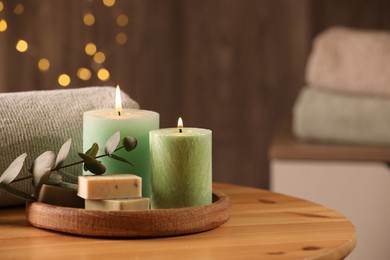 Photo of Spa composition. Burning candles, soap, towel and eucalyptus branch on wooden table, space for text