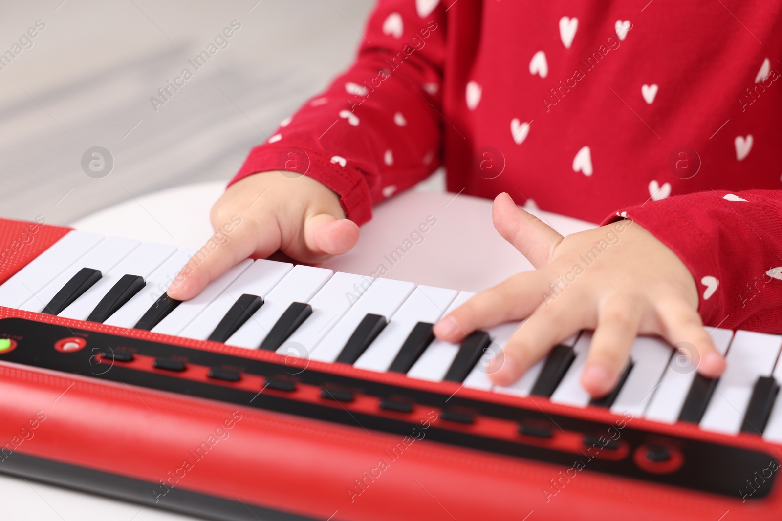 Photo of Little girl playing toy piano at home, closeup