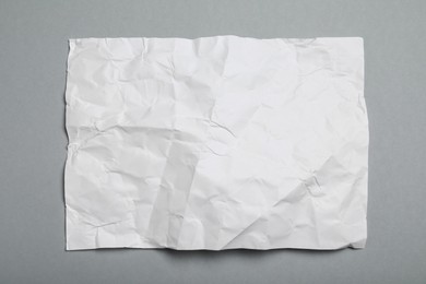 Sheet of white crumpled paper on grey background, top view