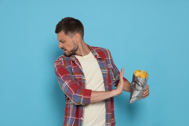 Handsome man refusing to eat potato chips on light blue background