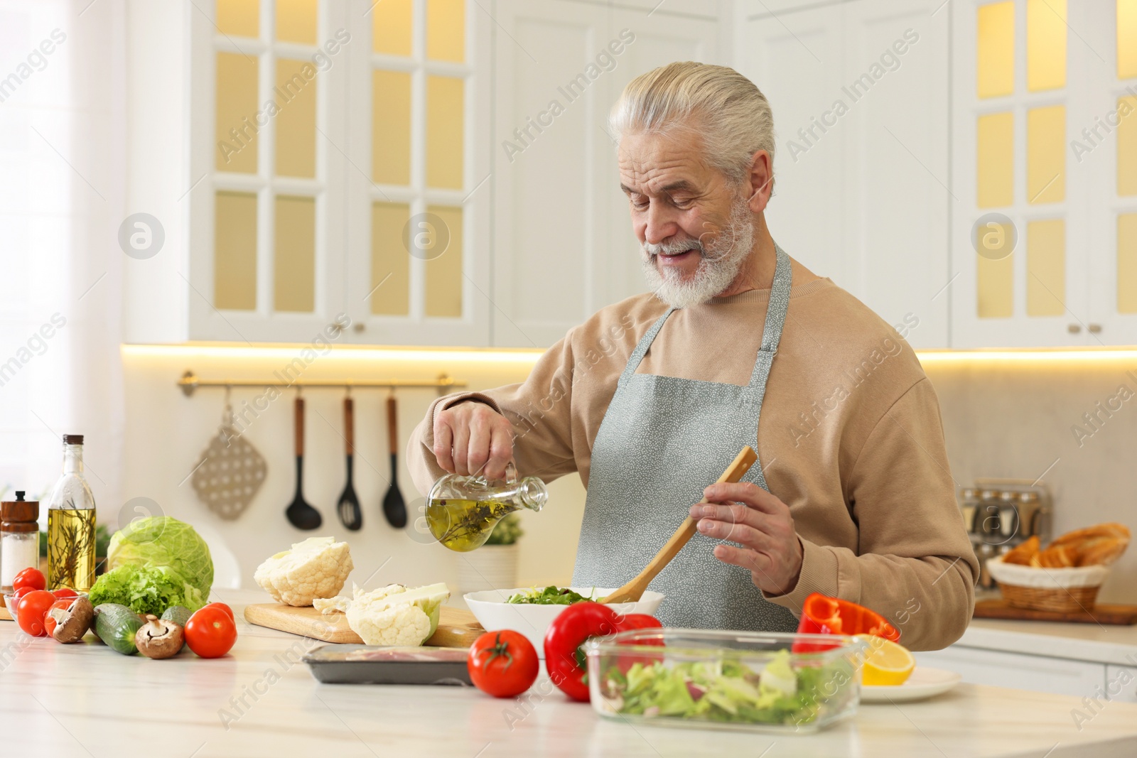 Photo of Man pouring oil into bowl with fresh salad at table in kitchen