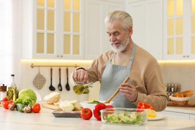 Man pouring oil into bowl with fresh salad at table in kitchen