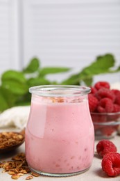 Photo of Tasty raspberry smoothie with granola in glass jar and fresh berries on light table, closeup