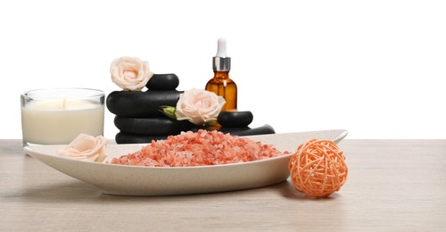Photo of Natural sea salt in bowl and other spa supplies on wooden table against white background