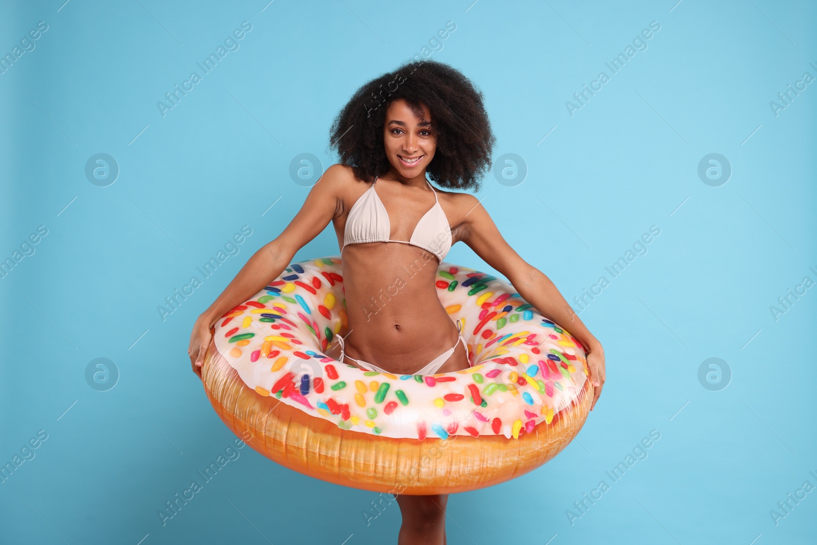 Photo of Beautiful woman in stylish bikini with inflatable ring on light blue background