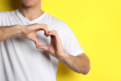 Man making heart with hands on yellow background, closeup. Space for text