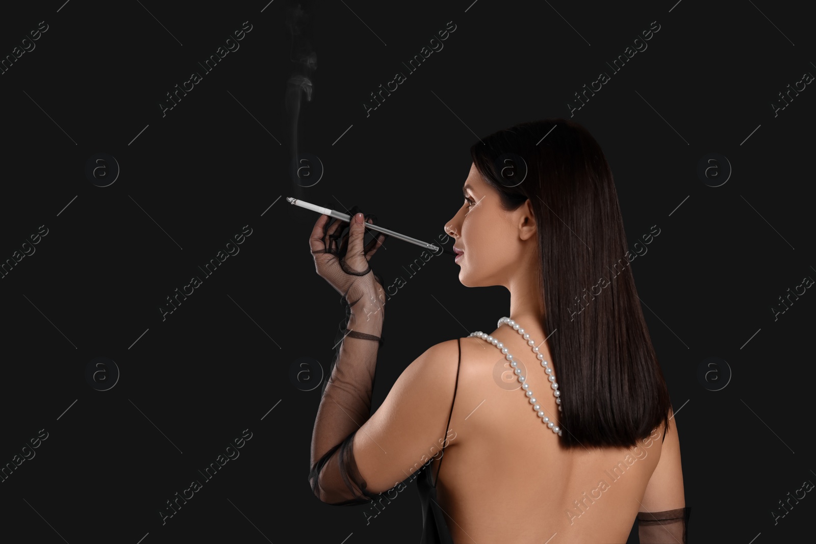 Photo of Woman using long cigarette holder for smoking on black background, space for text