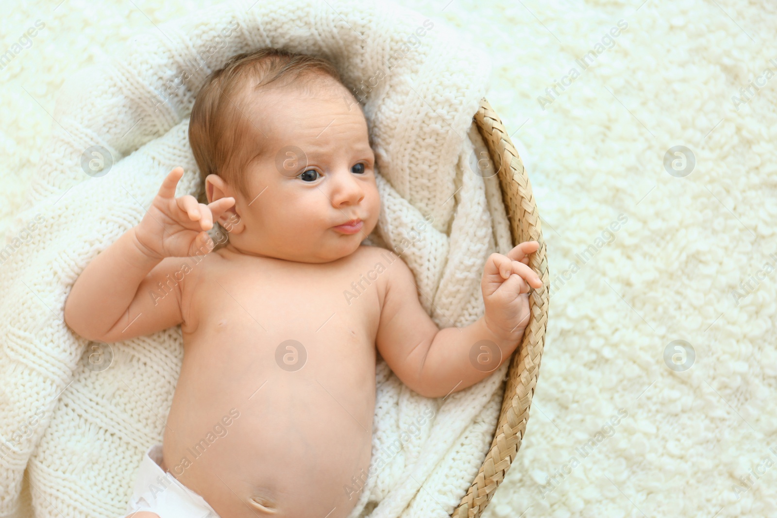 Photo of Cute little baby lying on knitted plaid in cradle, top view. Space for text