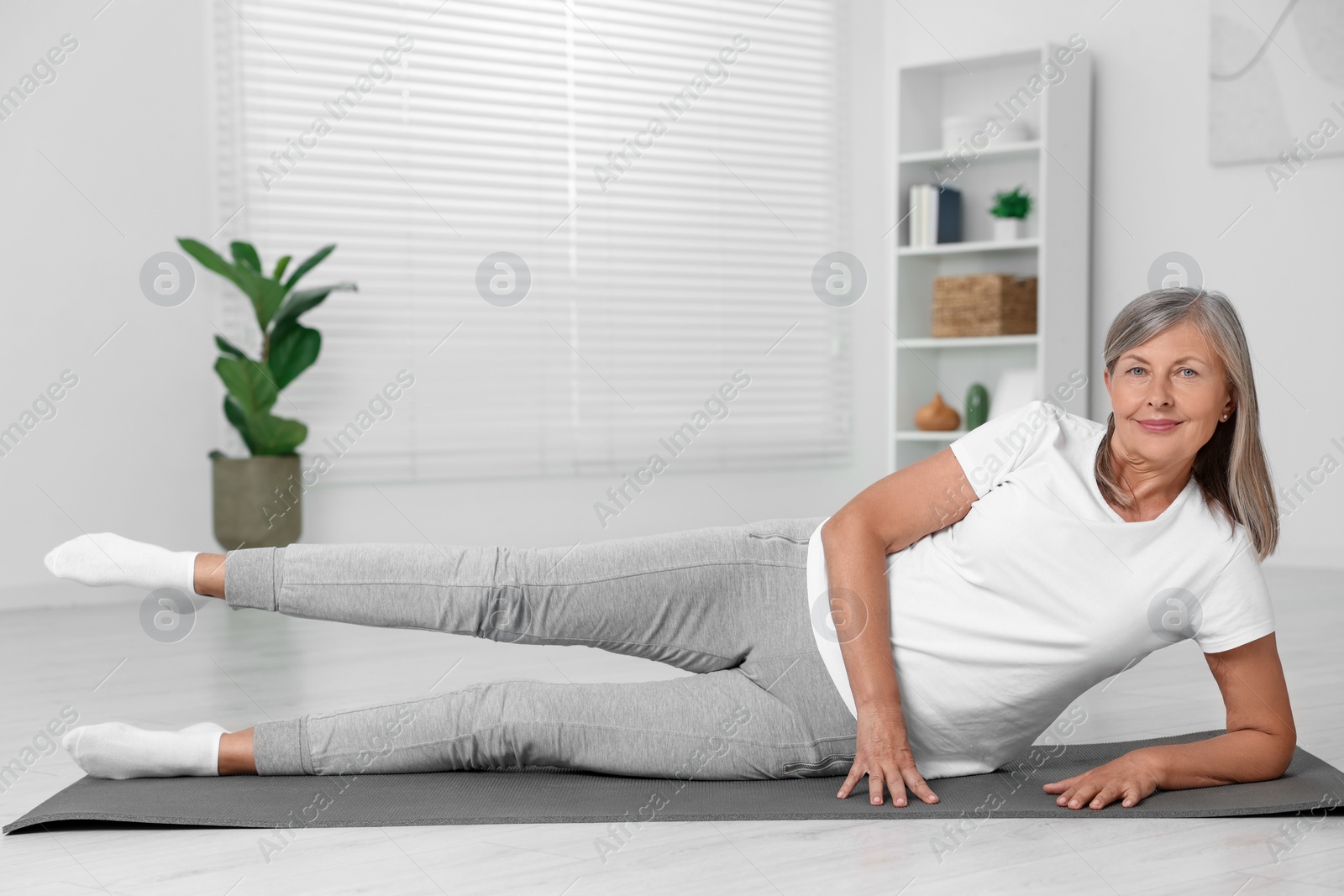 Photo of Happy senior woman practicing yoga on mat at home