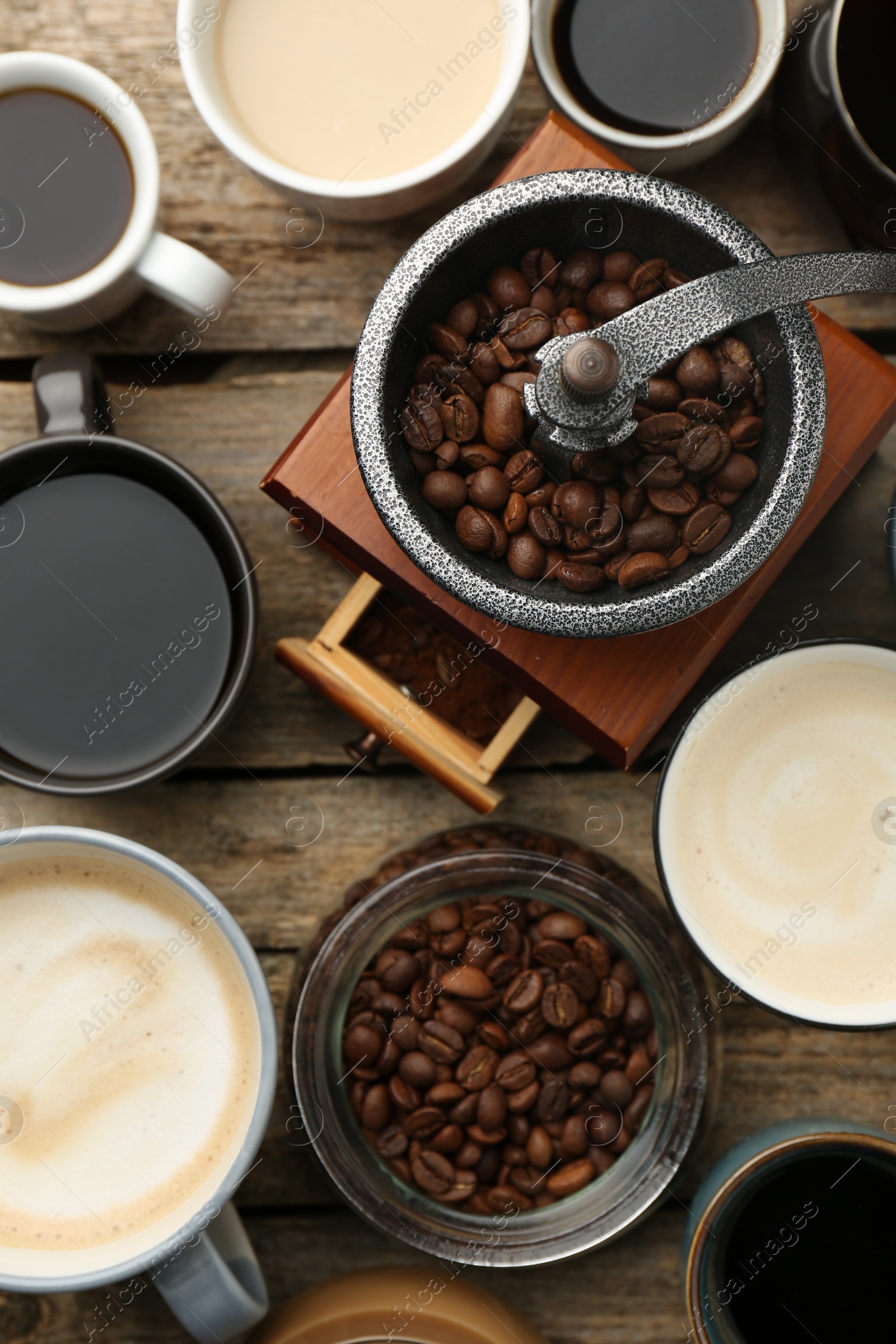 Photo of Different coffee drinks in cups, beans and manual grinder on wooden table, flat lay