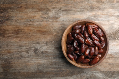 Bowl of sweet dates on wooden background, top view with space for text. Dried fruit as healthy snack