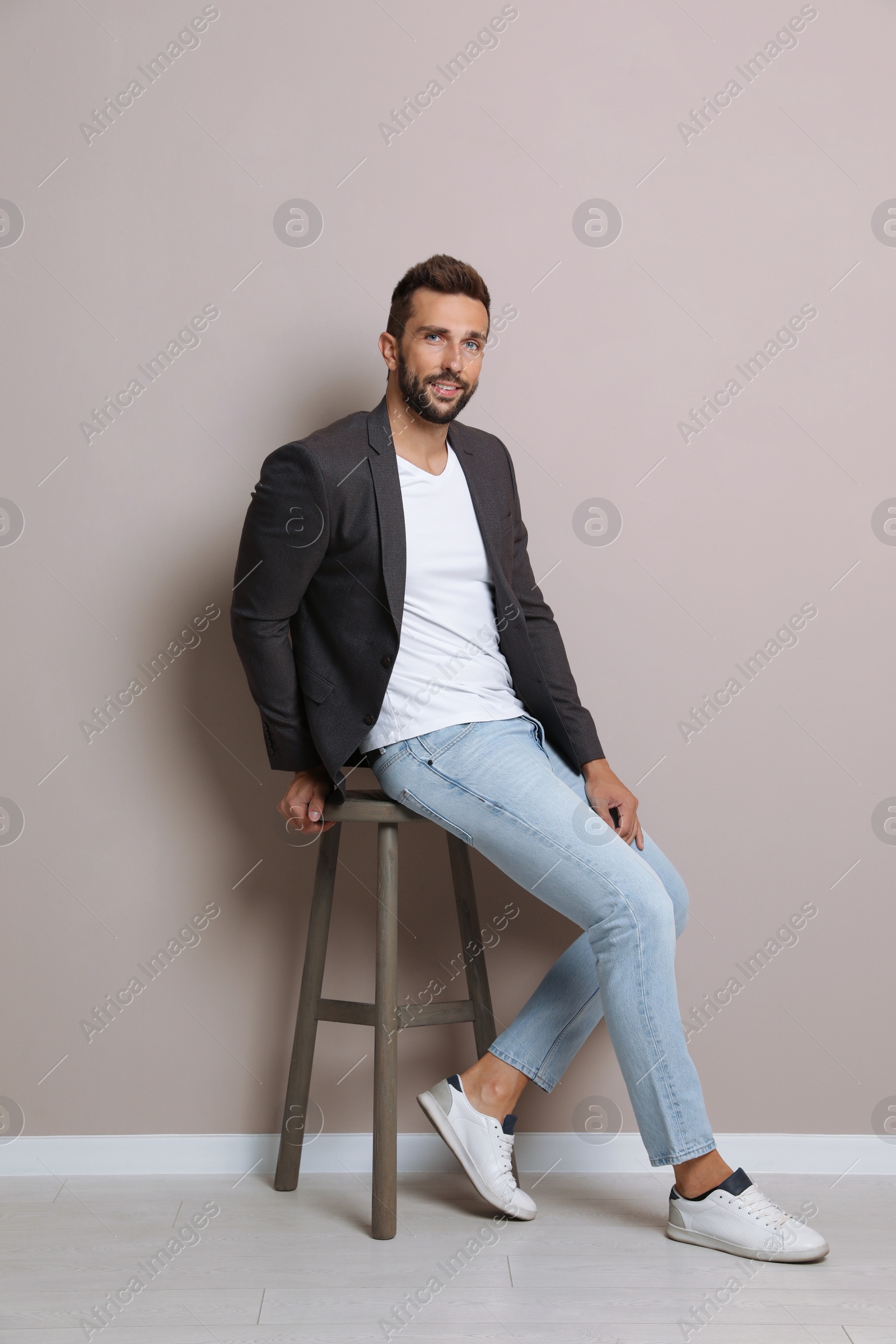 Photo of Handsome man sitting on stool near beige wall